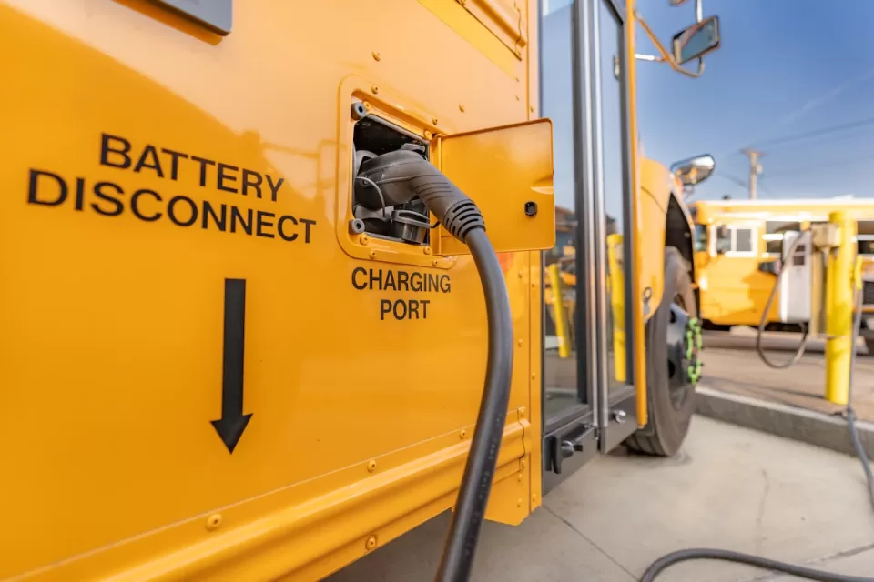 Close-up of charging port on yellow electric school bus plugged in at charging station.